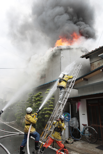 黒煙を上げて燃える民家を消火する消防隊員