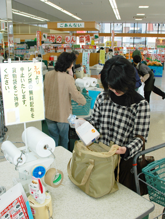 持参したバッグに購入商品を入れる買い物客