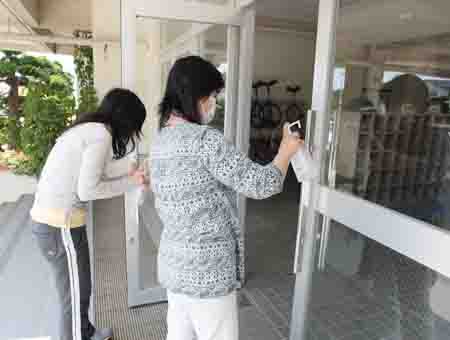 週明けから児童の登校再開に向けて玄関ドアの取っ手を消毒する学校職員
