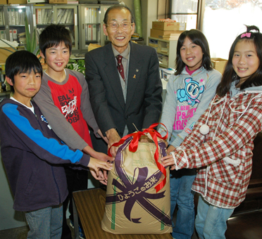 収穫したもち米を市社会福祉協議会の中山茂雄理事長=中央=に渡した児童たち