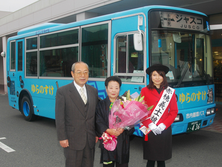 運行開始から4年3カ月で利用者10万人に達した市内循環バス「ゆらのすけ」と節目の乗客になった高橋智恵子さん=中央