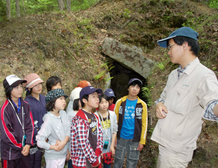 古墳の前で学芸員の説明を聴く児童たち