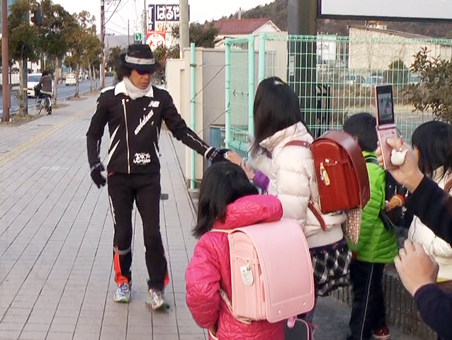 沿道で応援する子どもたちと握手を交わす間寛平さん