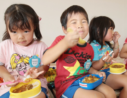 収穫野菜で調理したカレーライスをほおばる子どもたち