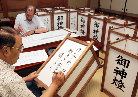 俳句を行燈に毛筆書きして献納に備える片山青芝さん=手前=と大西平八郎さん