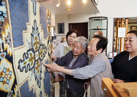 阪口キリヱさん=左から2人目=と広門マツエさん=同3人目=から赤穂緞通の作品評価を受ける井関京子さん=右端=ら花工房のメンバー