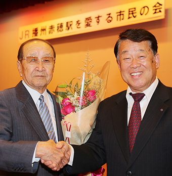 新会長の飯尾義明氏(右)と10年間の功労に花束を贈られた寒川信男・名誉会長