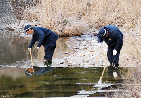 現場近くの川を捜索する捜査員