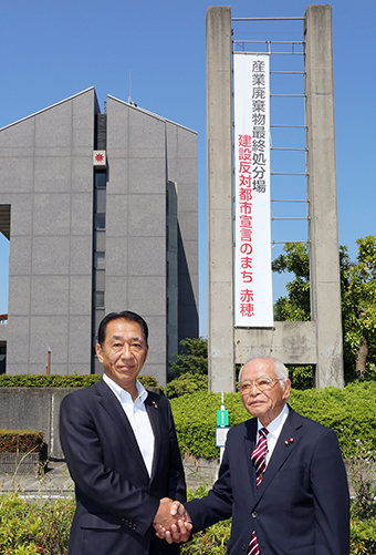 懸垂幕をバックに「産廃処分場建設反対」を誓い合った家入時治議長(左)と「市民の会」の木村音彦会長