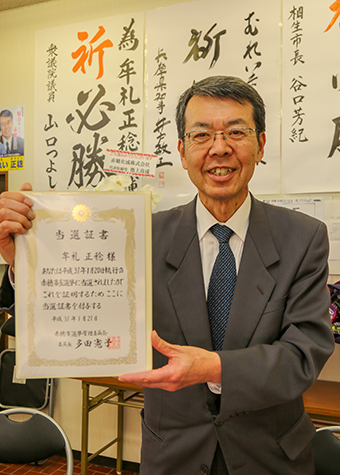 当選証書を手に「粉骨砕身取り組む」と決意を語る牟礼正稔氏