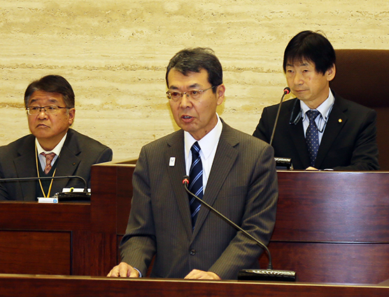 就任初年度の施政方針を述べる牟礼正稔市長=右は瓢敏雄議長、左は柳生信・議会事務局長