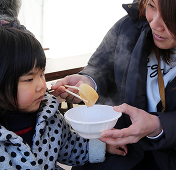 湯気がたつ「厄除け大根」を食べる親子連れ