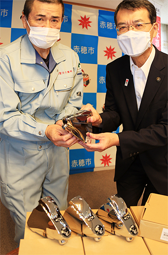 牟礼正稔市長に自動水栓蛇口を手渡す高橋勝己理事長(左)