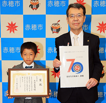 70周年記念シンボルマークを発表する牟礼正稔市長とキャッチフレーズを考案した森谷晃大君