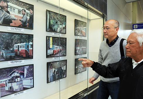 明神電車の展示写真を小林史朗会長(左)に案内する吉栖清美さん